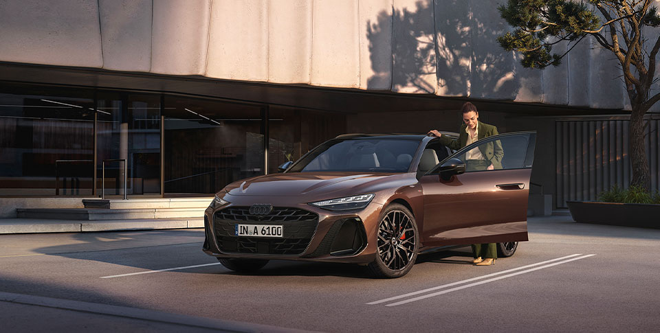 Frontansicht des neuen Audi A6 mit Business-Frau, auf Asphalt vor modernem Geb&auml;ude