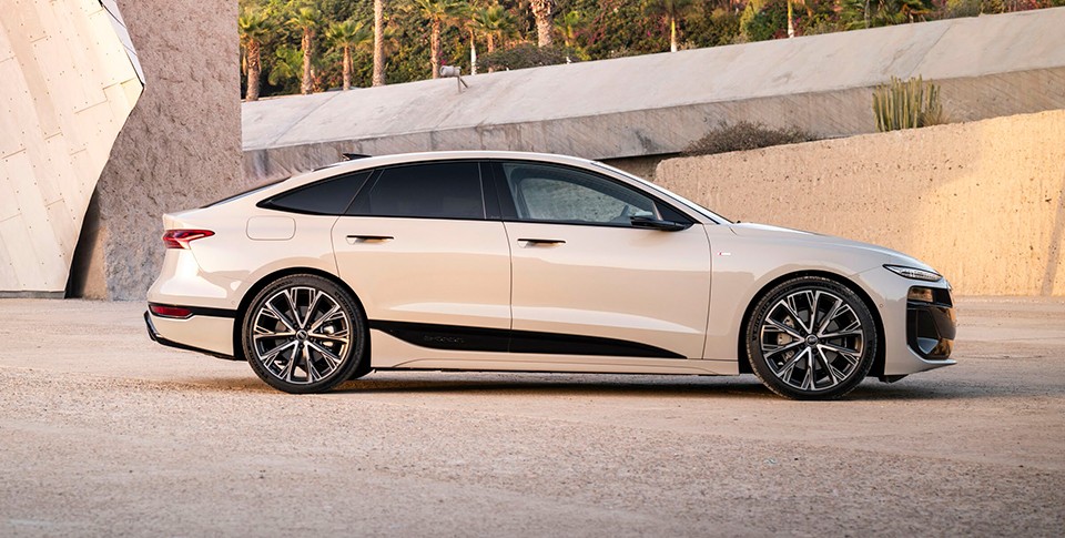 Seitenansicht eines beiges Audi A6 Sportback e-tron auf beigem Untergrund vor moderner Stein-Holz Kulisse