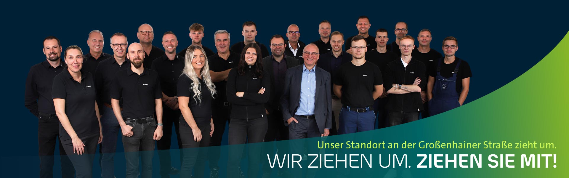 Mitarbeiter-Gruppe, bestehend aus 24 Menschen, steht vor einem blauen Hintergrund mit dem Slogan 'Wir ziehen um. Ziehen Sie mit!'